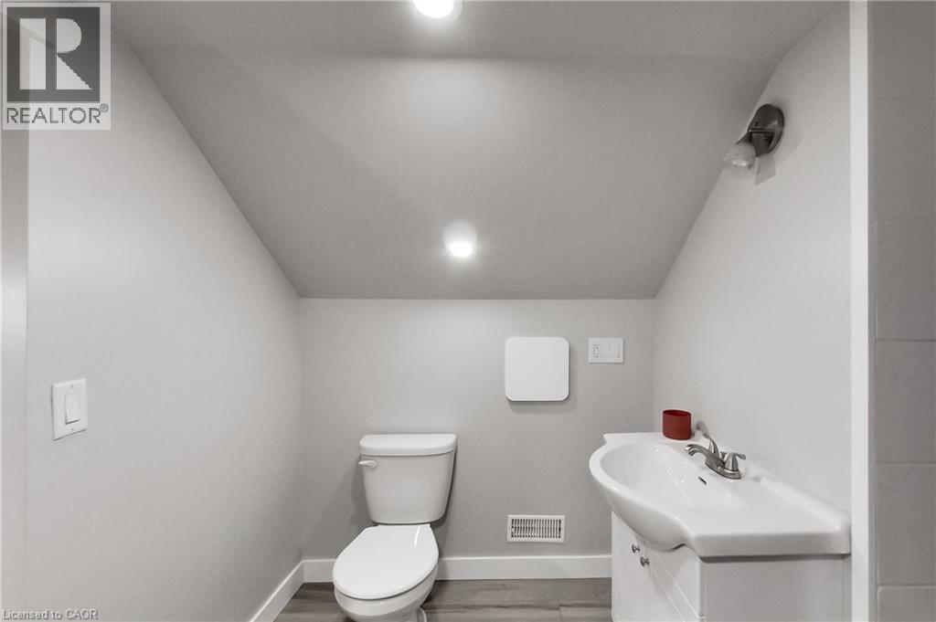Recessed ceiling lighting, angled ceiling, white toilet, wall-mounted vanity light, wood-finish flooring