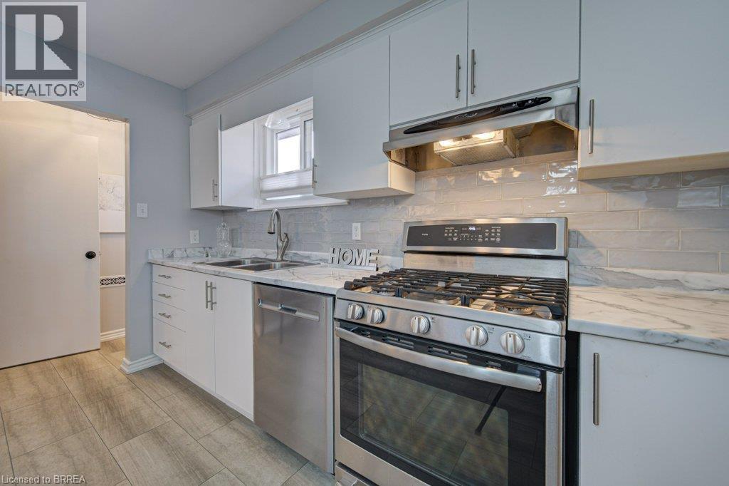 Kitchen featuring stainless steel appliances, wood-finish flooring, white cabinetry with silver hardware, light-toned backsplash, and a double basin sink