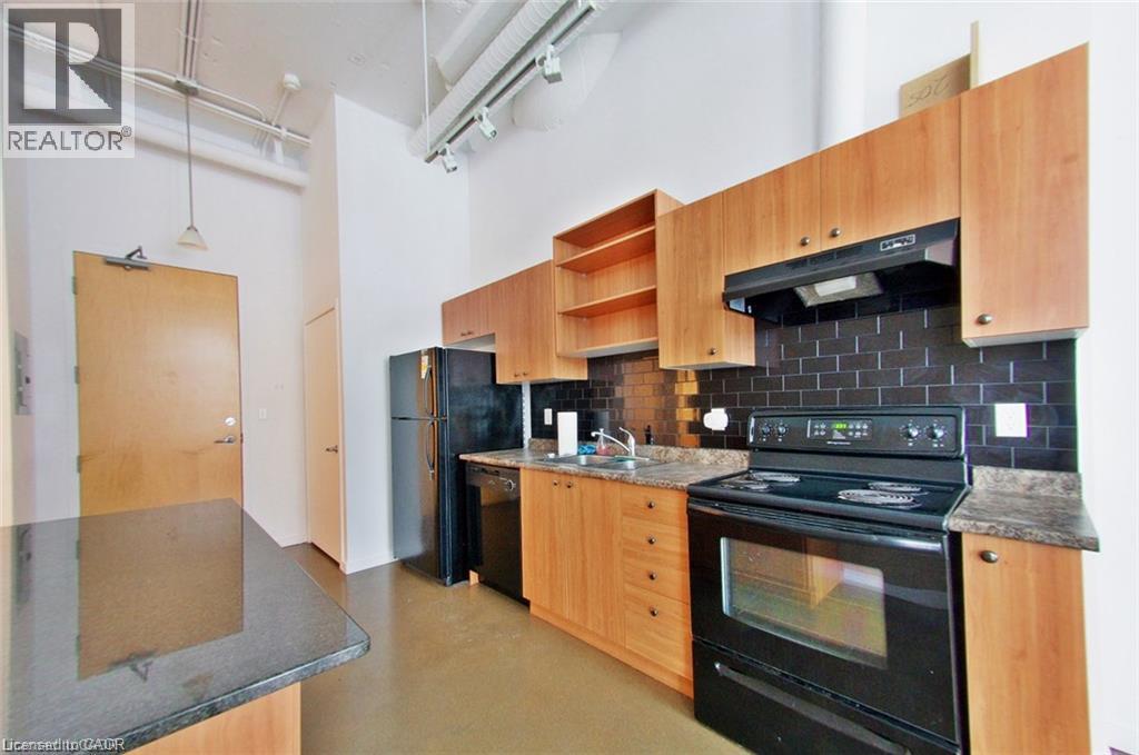 Kitchen featuring wood-finish cabinetry, black subway tile backsplash, black appliances, and dark speckled countertops