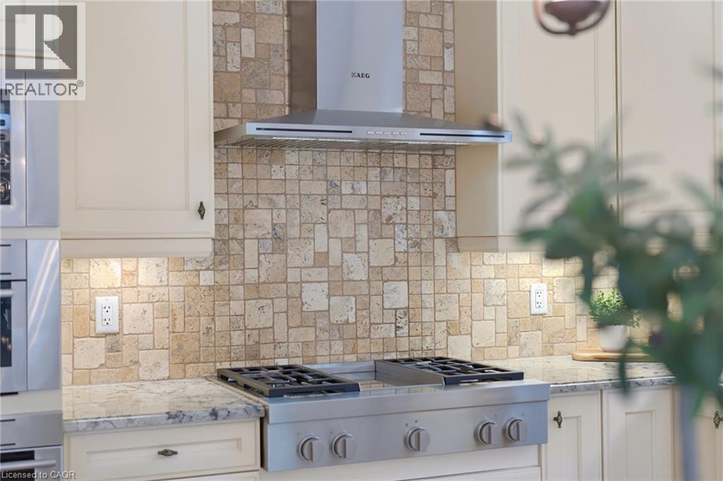 Cream cabinetry, mosaic tile backsplash, stainless steel range hood, built-in cooktop with grates, and light-toned countertops