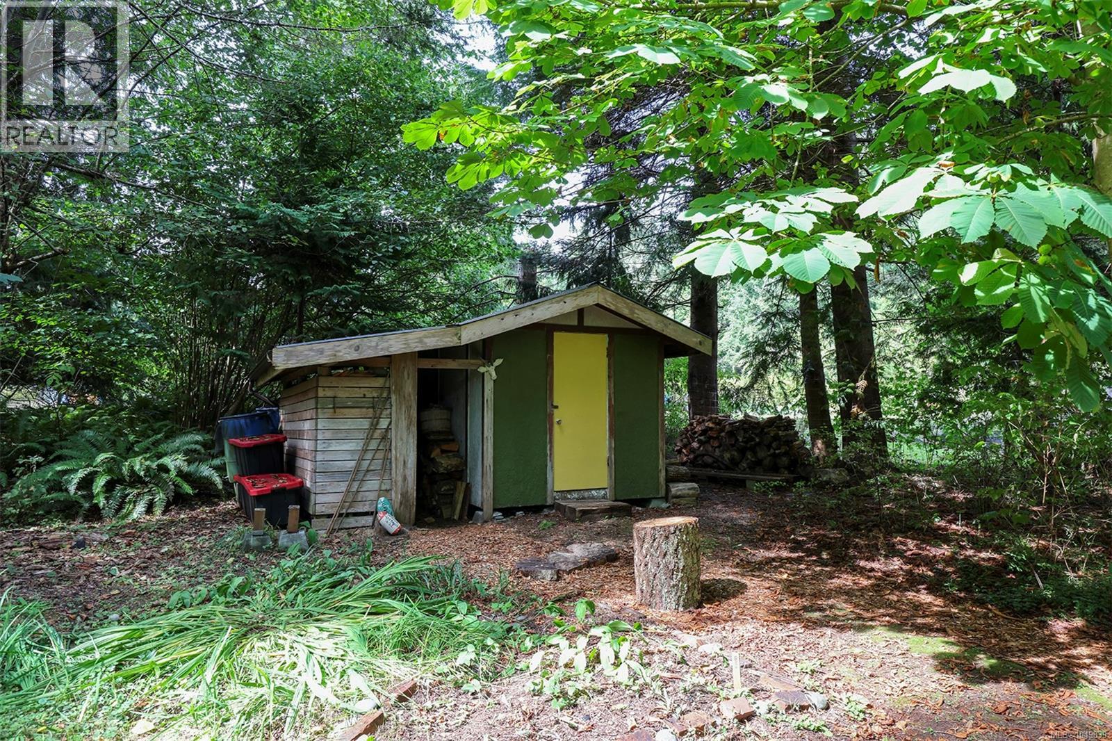 Green storage shed with a yellow door, featuring an attached lean-to for firewood