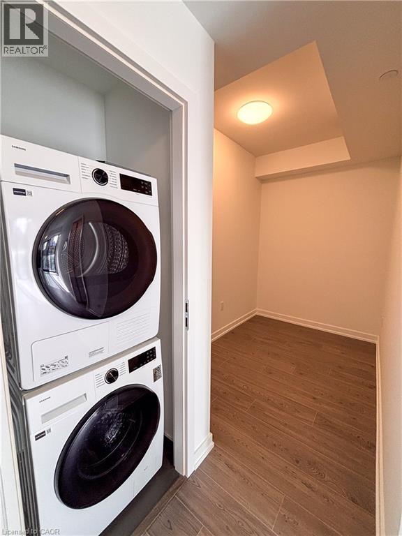 Stacked washer and dryer units, wood-finish flooring, recessed ceiling light, white wall finishes