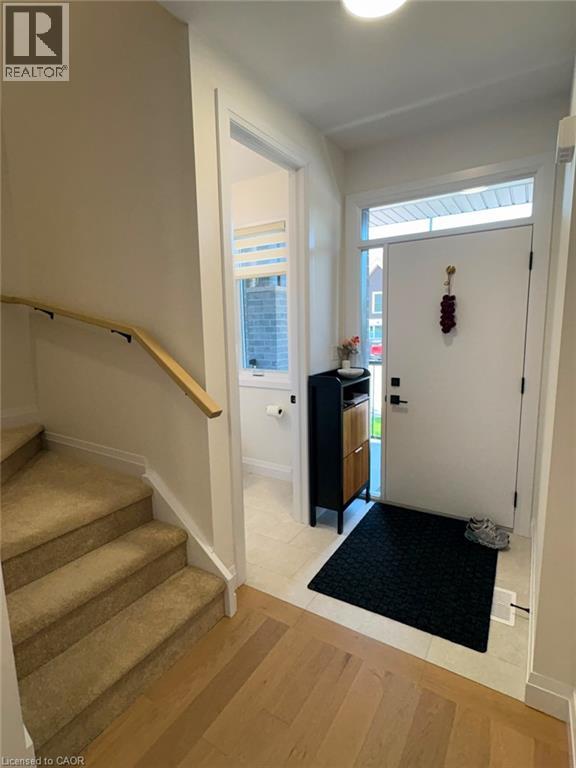 Entryway featuring wood-finish flooring, a carpeted staircase with a wood handrail, and a white entrance door with an overhead transom window