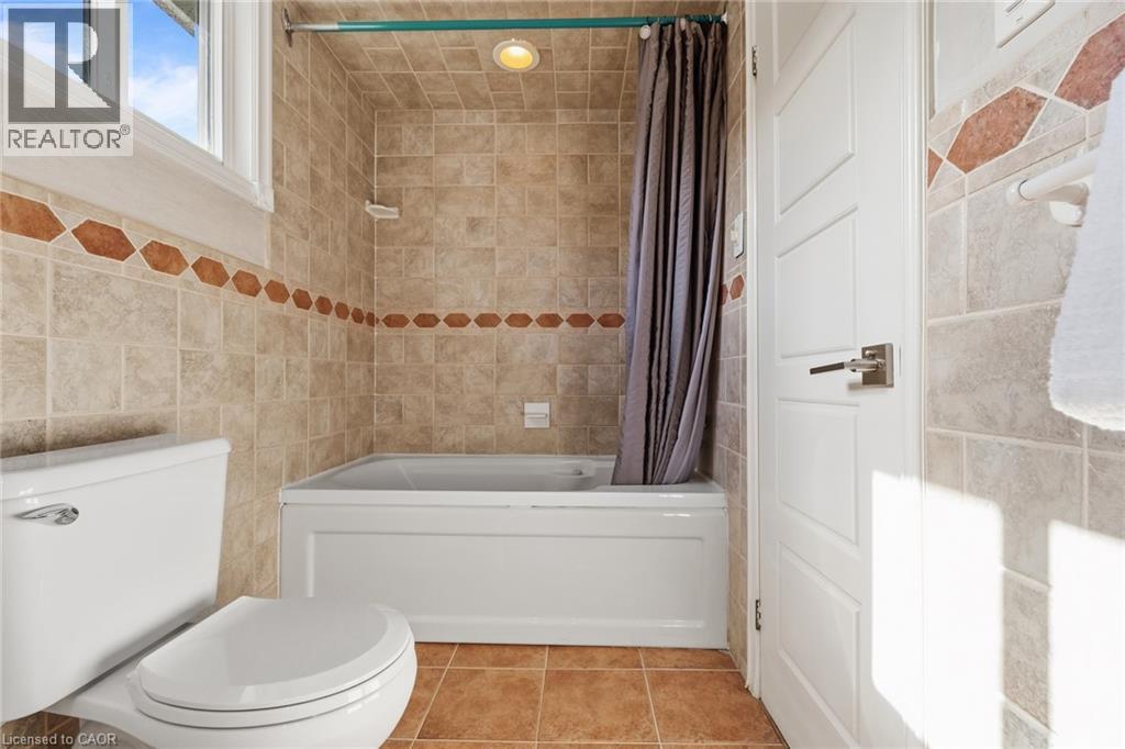 White panel door with satin nickel hardware, ceramic tile flooring, and tiled shower surround with decorative accent band