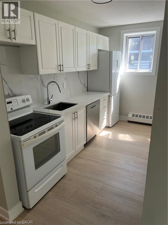 Kitchen featuring white upper and lower cabinetry, a stainless steel sink with a high-arc faucet, and wood-finish flooring