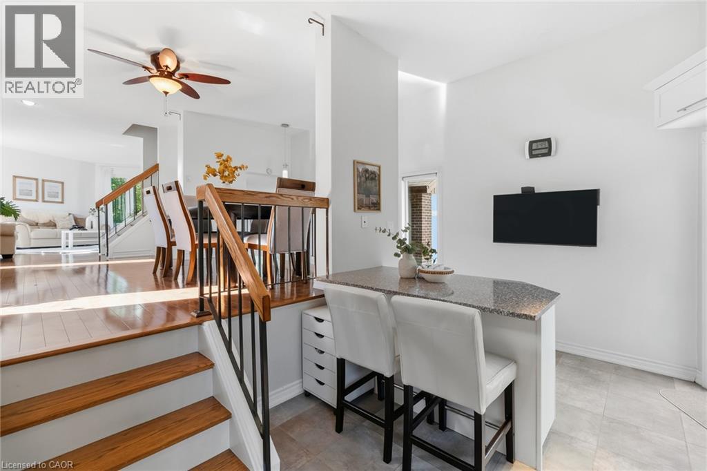 Multi-level interior featuring wood-finish flooring, a contemporary staircase with wood handrails and black metal spindles, a ceiling fan with integrated lighting, and a kitchen island with a light-to