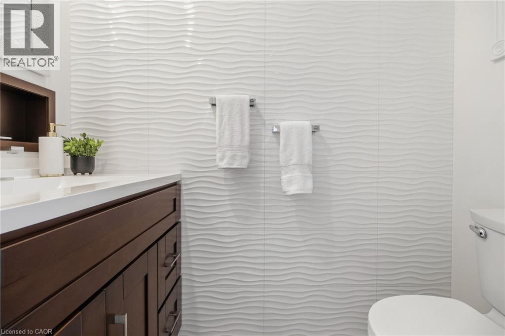Wavy textured wall tile, wood-finish vanity with an integrated sink, built-in shelving, and sleek towel bars