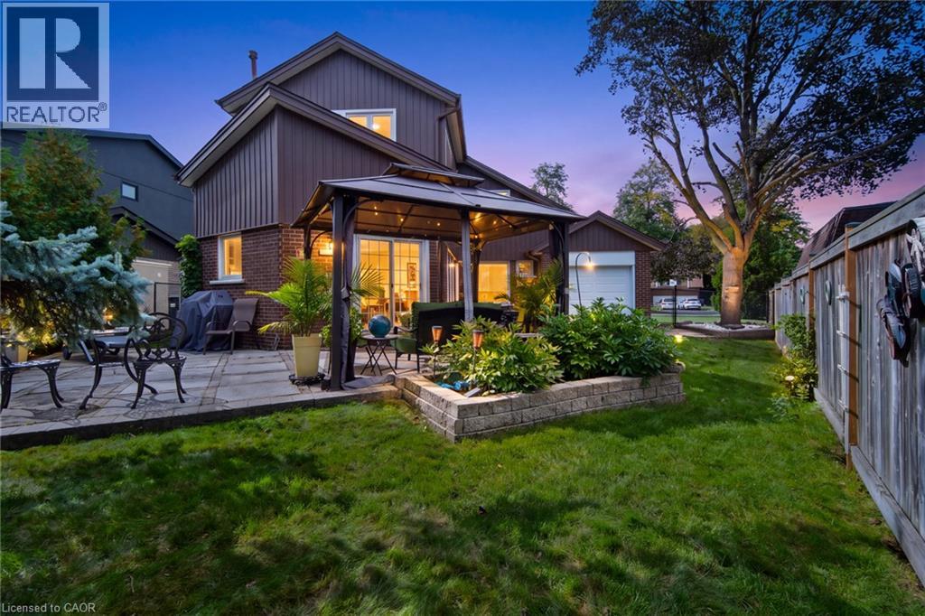 Expansive backyard featuring a stone paver patio, integrated gazebo with string lighting, a raised garden bed, and mature trees