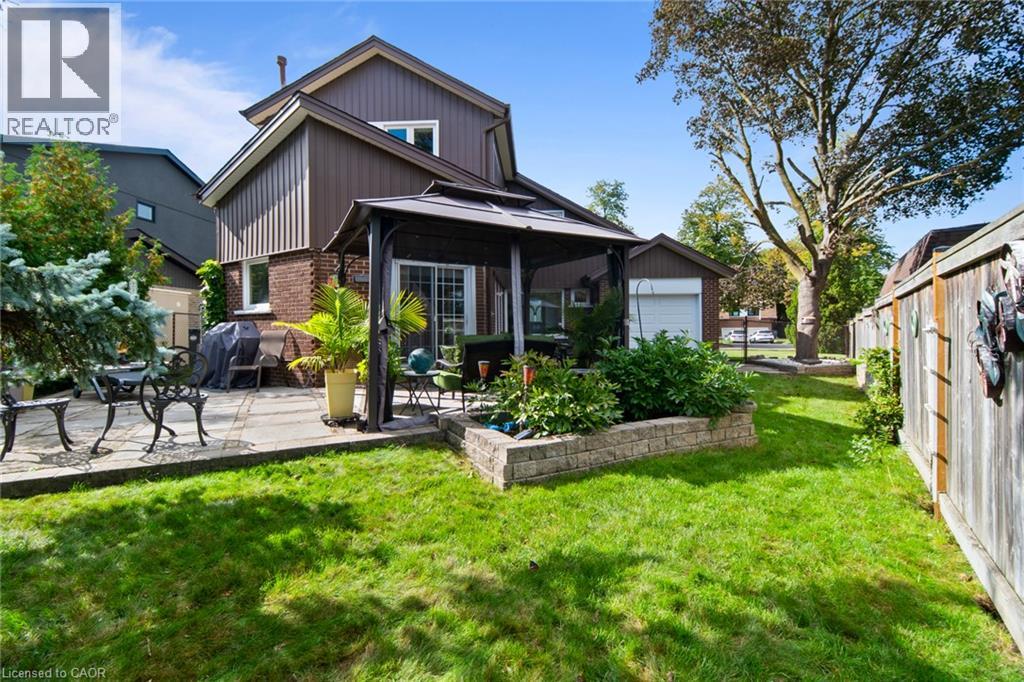 Expansive backyard featuring a stone patio, mature trees, a built-in garden bed, wood fencing, and a detached garage
