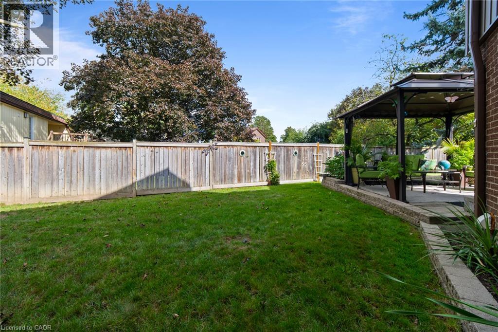 Expansive lawn area with a wood privacy fence, featuring a paved patio with a gazebo structure and a stone retaining wall