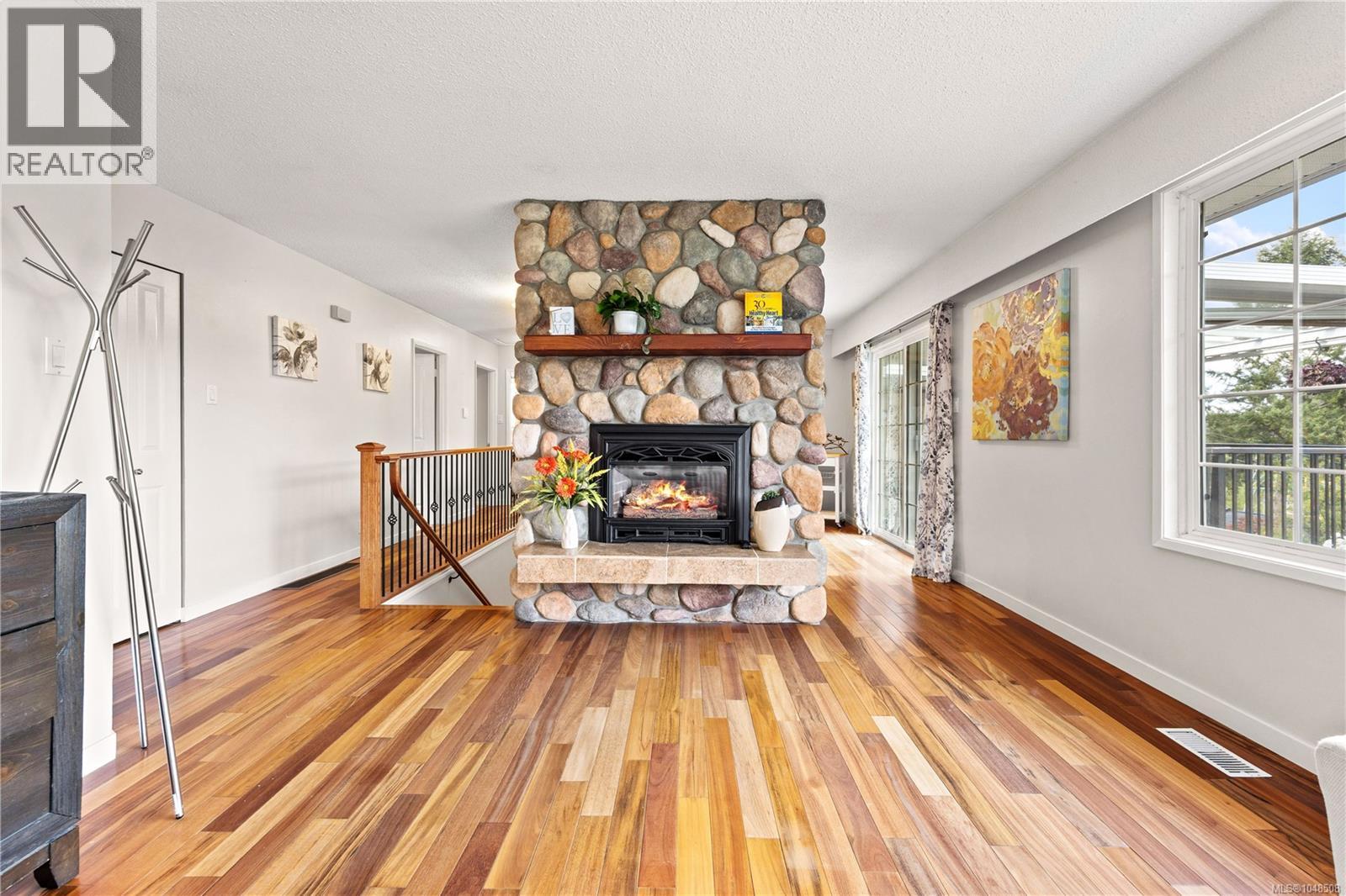 Hardwood flooring throughout, stone fireplace with a wood mantle, sliding glass door, and large window