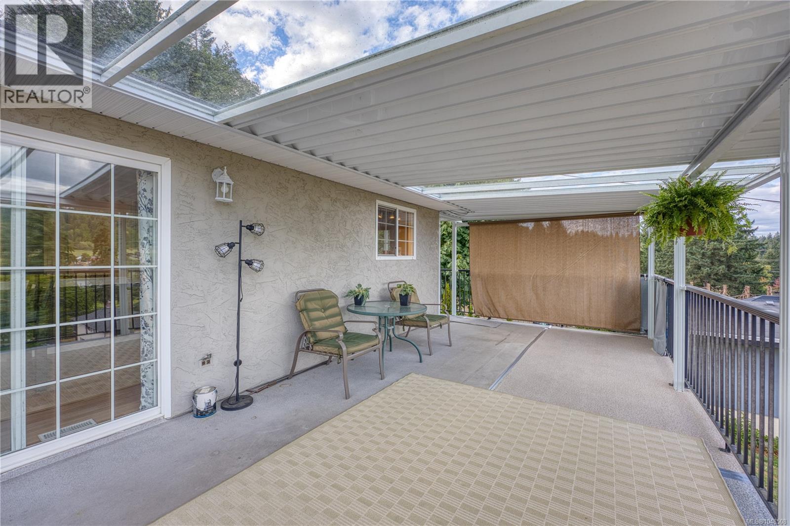 Covered outdoor patio with a concrete surface, featuring a railing, wall-mounted light fixture, and sliding glass door access