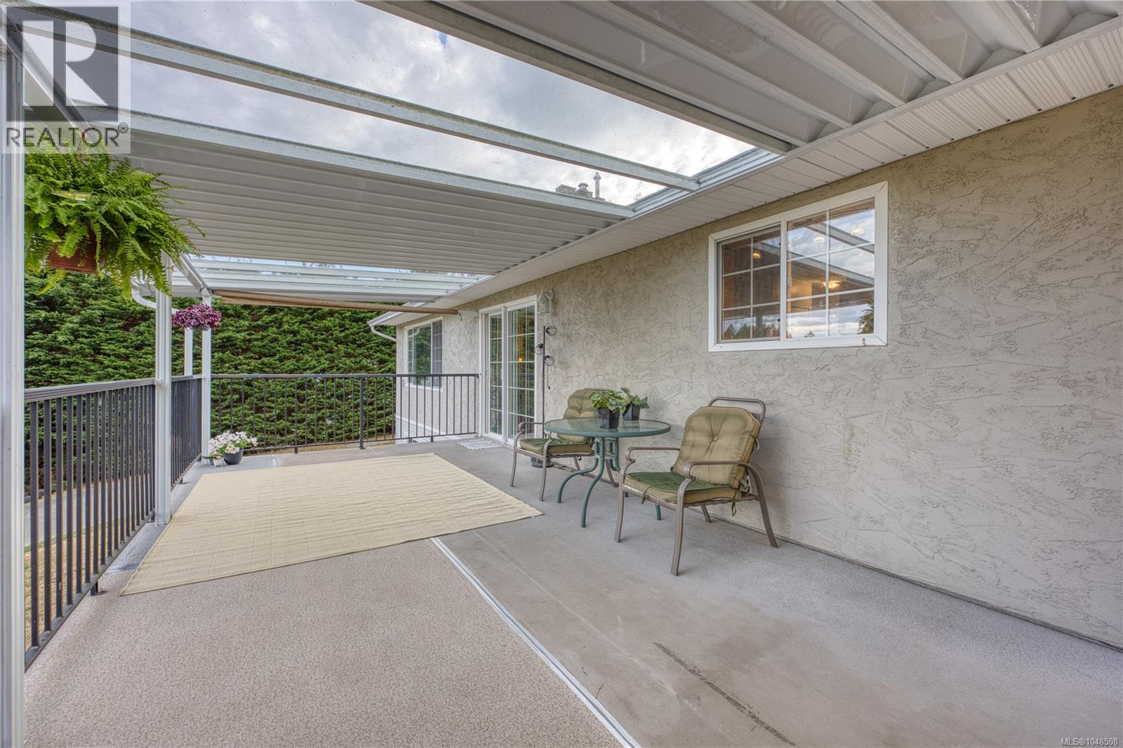 Covered concrete patio featuring an aluminum frame roof with transparent panels, a sliding glass door, and a white-framed window