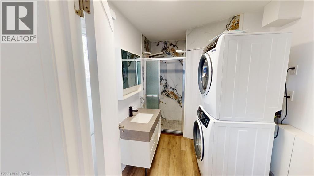 Contemporary bathroom featuring a floating vanity with a vessel sink, a stacked washer and dryer, a glass-enclosed shower with marble-look wall tiling, and wood-finish flooring
