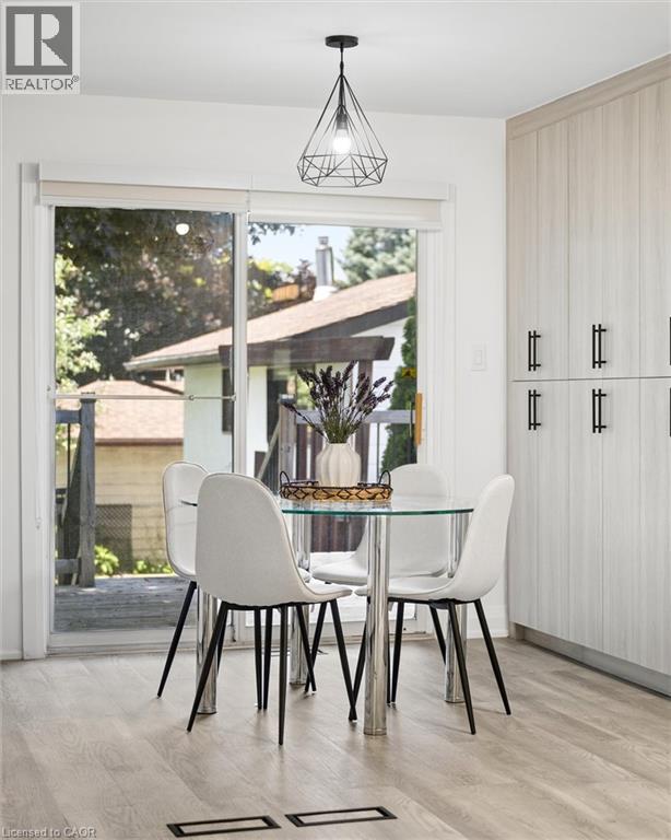 Eat-in kitchen area featuring a glass-top table, wood-finish flooring, full-height cabinetry with black pulls, and a geometric pendant light fixture