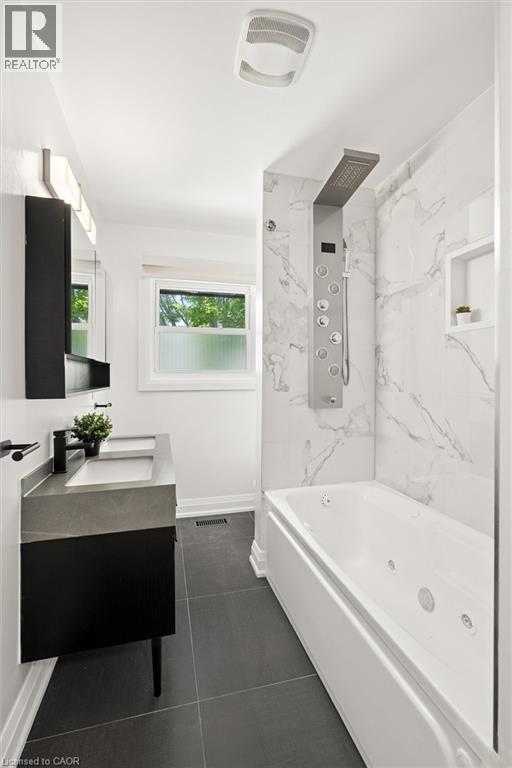 Modern bathroom featuring a jetted tub, a multi-function shower panel, and a wall-mounted vanity with an integrated sink