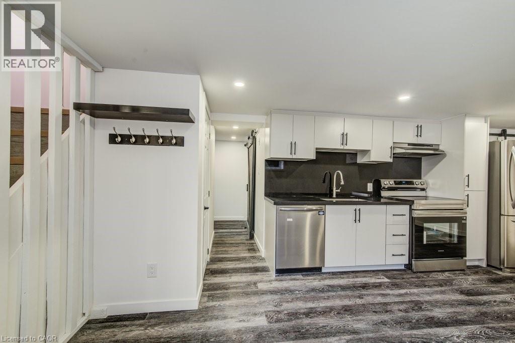 Compact kitchen featuring white cabinetry, stainless steel appliances, a matte black faucet, dark countertops, and wood-finish flooring