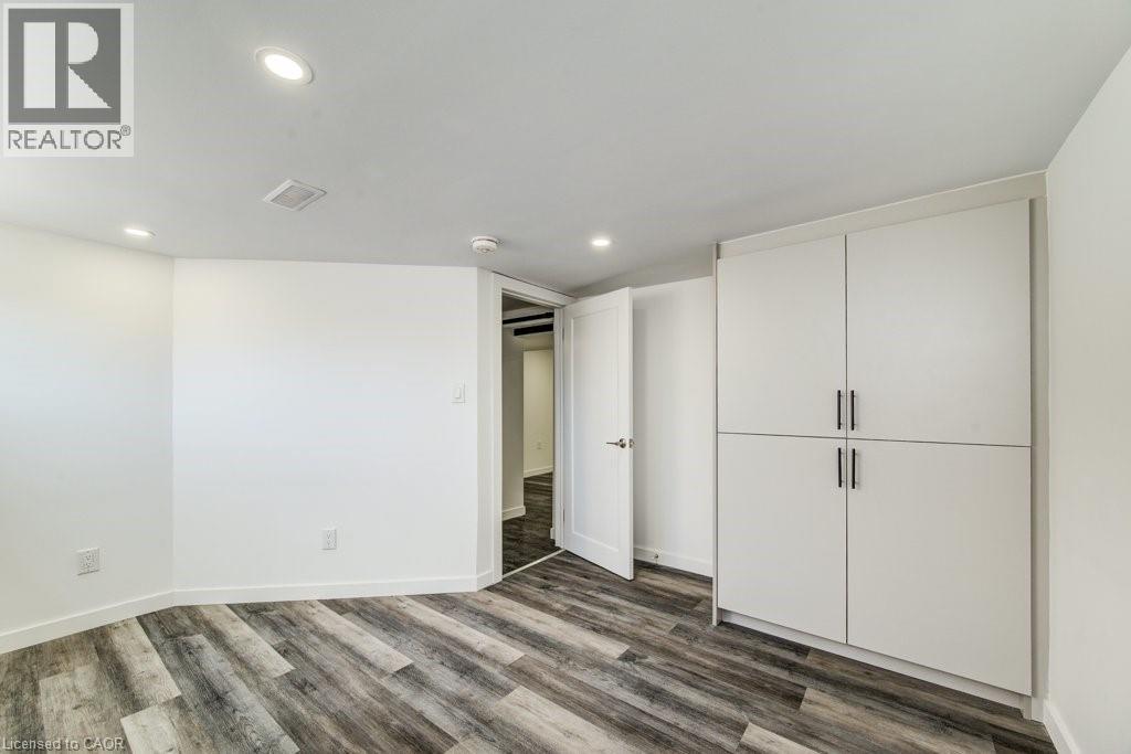 Room featuring wood-finish flooring, recessed lighting, white walls, and built-in cabinetry with dark hardware