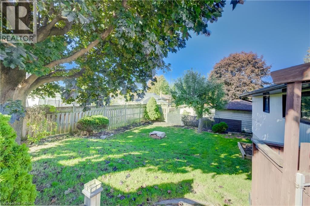 Expansive green lawn with mature shade trees, bordered by a wooden privacy fence